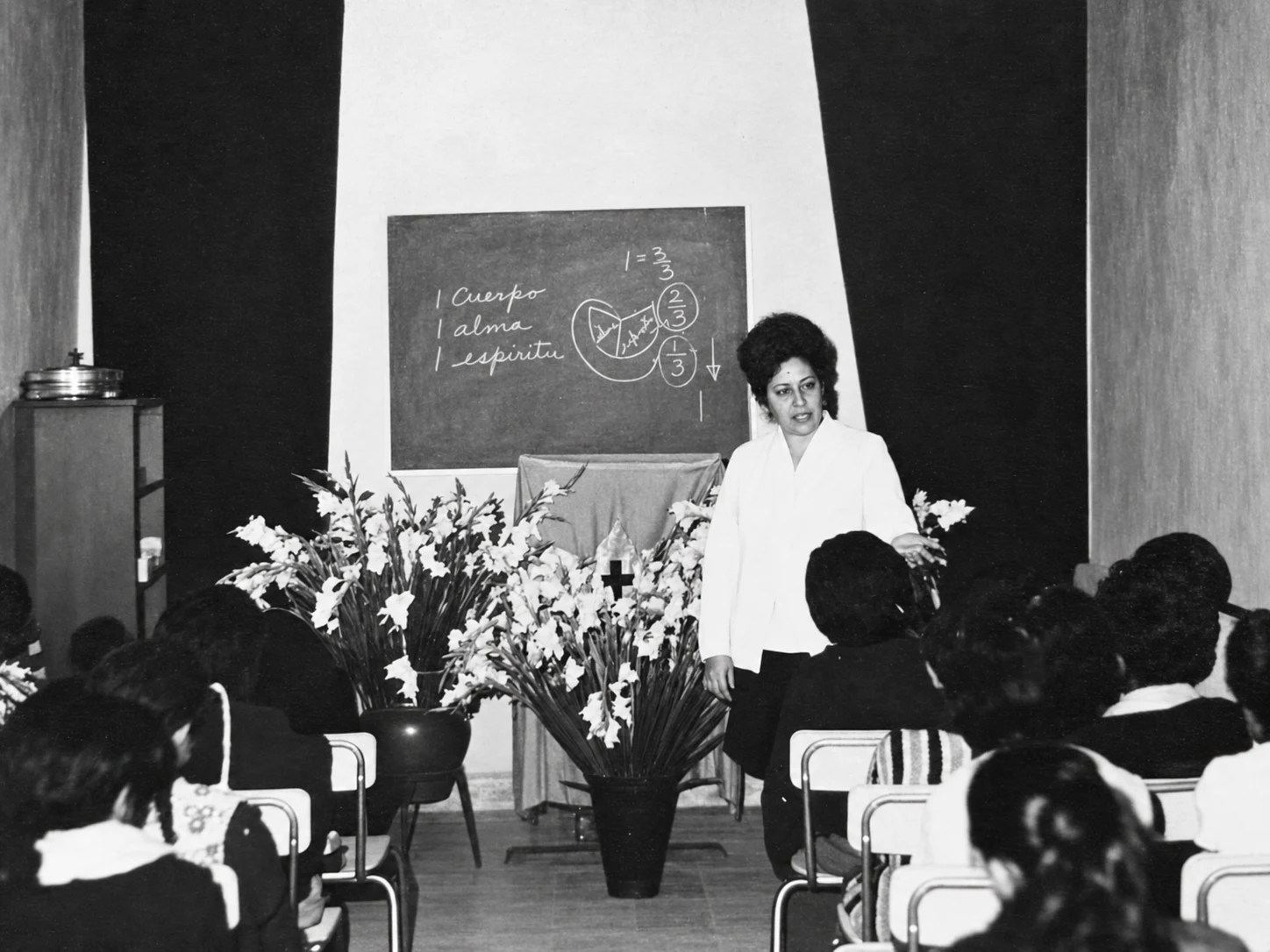 Fotografía histórica de una mujer compartiendo la Palabra ante la congregación